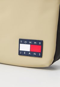Borsa morbida beige con superficie testurizzata; presenta un logo rettangolare in blu navy, rosso e bianco con la scritta "TOMMY JEANS".