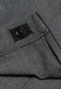 Tessuto grigio con una texture sottile, dotato di un bottone nero e di una cerniera lungo il bordo. Particolari delle cuciture visibili, che indicano la qualità della lavorazione.