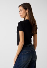 Czarna bawełniana koszulka z krótkimi rękawami, noszona z niebieskimi jeansami. Koszulka ma prosty krój i luźne dopasowanie, bez widocznych wzorów.