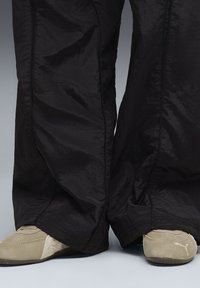 Pantaloni neri, leggeri e strutturati, con una vestibilità ampia, abbinati a calzature beige simili al camoscio con un logo. Ribattiture nere lungo i bordi dei pantaloni.