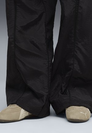 Schwarze, leichte, strukturierte Hose mit lockerem Sitz, kombiniert mit beigem, samtartigem Schuhwerk mit Logo. Schwarze Bordüre entlang der Kanten der Hose.