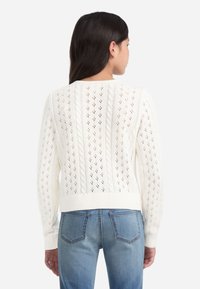 Valkoinen neulepusero, jossa on avoin boordikuvio ja palmikkoneulekorostukset sekä ribbireunukset hihansuissa, helmassa ja kauluksessa. Rentouttava, lyhyt malli.