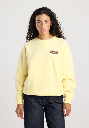 Sweatshirt jaune à coupe ample, avec des poignets côtelés et un col rond. Présente un texte brodé "5TH AVENUE BREAKFAST" sur le devant.