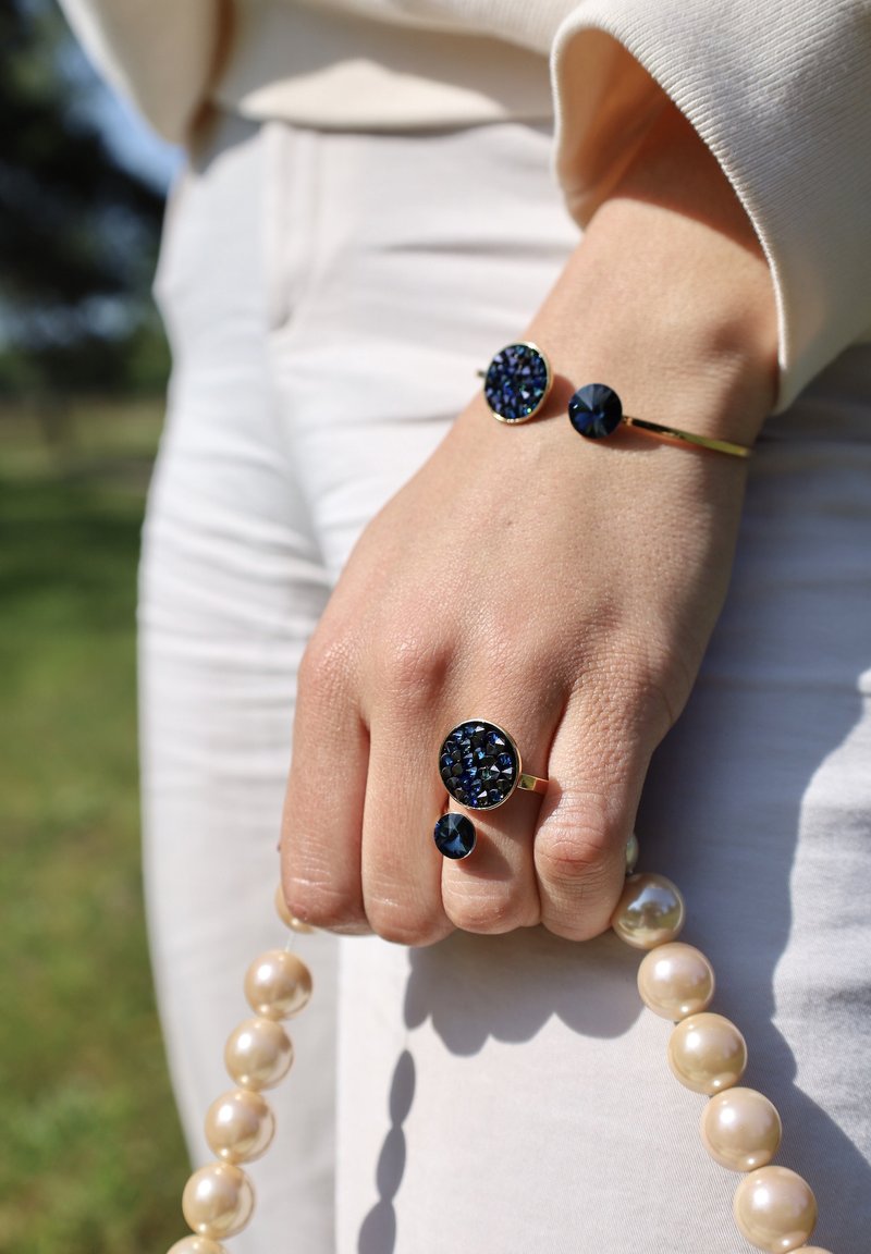 Marineblauwe edelstenen ring met gouden accenten, vergezeld van een bijpassende armband en een string grote, glanzende parelrozen.