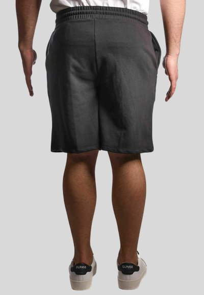 Pantaloni corti grigio scuro con vita elasticizzata, vestibilità ampia e tasche laterali, indossati con scarpe bianche con un accento nero sul tallone.