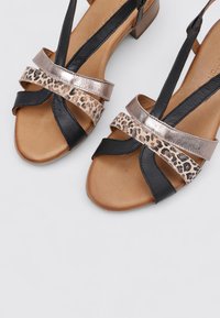 Sandales noires et métalliques avec des accents imprimés léopard, présentant des sangles croisées, un faible talon en bois et une texture en cuir lisse.