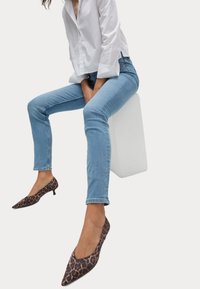 Jeans ajustados de un azul claro con una sutil textura de denim, combinados con zapatos de tacón de punta con un diseño de estampado de leopardo marrón.