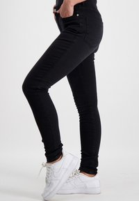 Zwarte skinny jeans van denim, met voor- en achterzakken, een ritssluiting, en gecombineerd met witte sneakers.