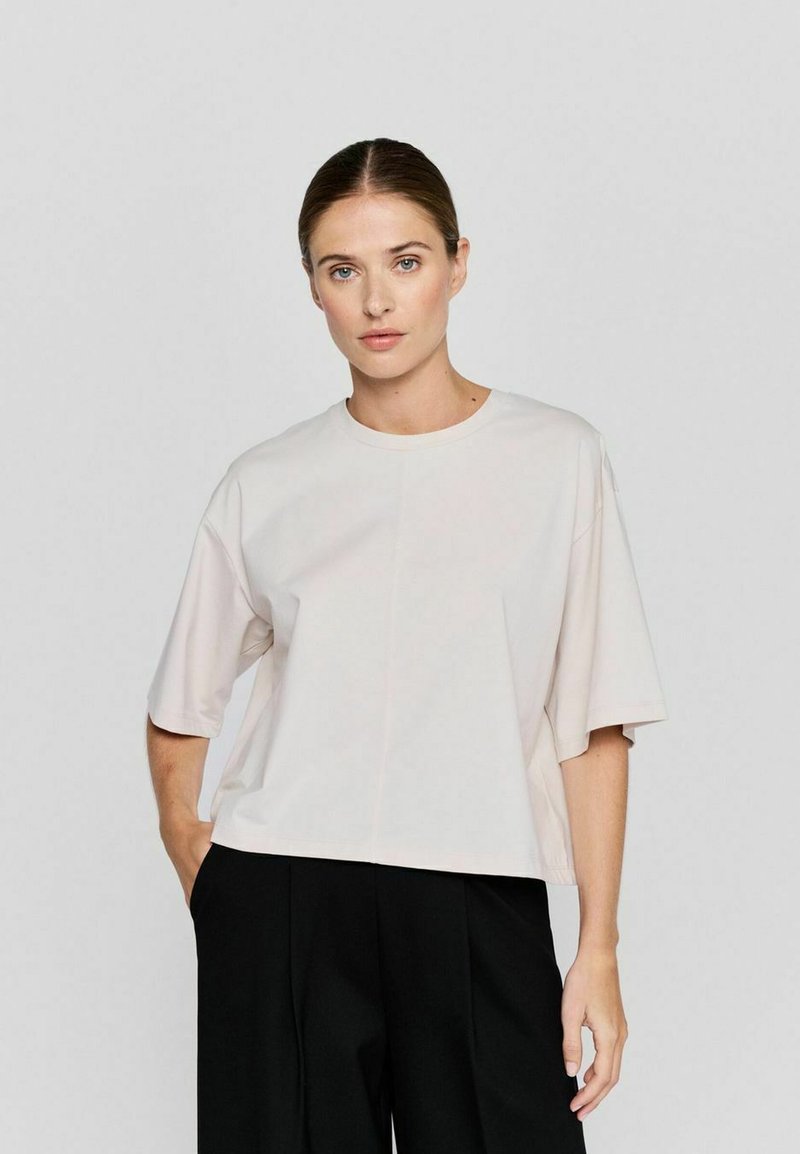Licht beige cropped t-shirt met brede korte mouwen, ronde halslijn en een gladde textuur, gecombineerd met zwarte loszittende broek.