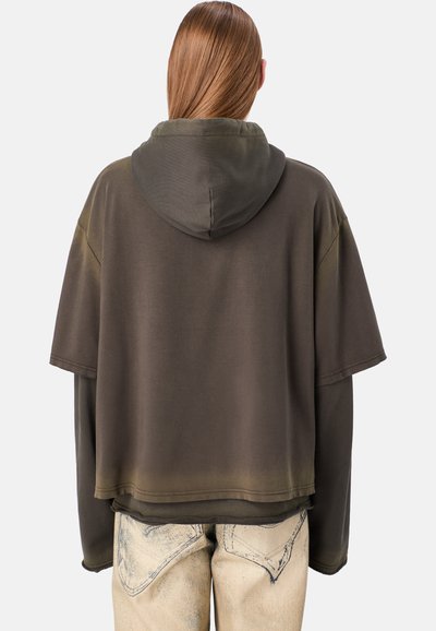 Felpa over-size con cappuccio di colore verde scuro con effetto sfumato, caratterizzata da maniche corte e tessuto morbido. Abbinata a pantaloni in denim chiaro, strappati.