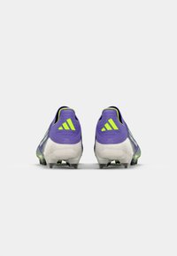 Lila Fußballschuhe mit grünen Akzenten, die ein schlankes Design, eine strukturierte Oberfläche und transparente Außensohlen mit Stollen für besseren Halt bieten.