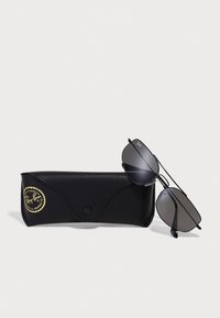 Caz de ochelari de soare din piele neagră cu un logo aurit, care conține ochelari de soare în stil aviator cu ramă metalică și lentile închise la culoare.