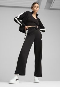 Mustar musta spordikomplekt valgete külgriidega, valmistatud pehmest kangast. Sobiva lõikega jakil on kõrge krae ja pükstel on elastne vöökoht.