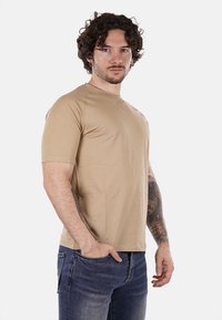 T-shirt beige a maniche corte realizzato in morbido tessuto con scollo rotondo e maniche raglan, abbinato a jeans denim blu.