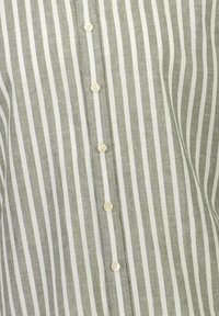 Lichtgewicht linnen shirt met verticale grijs-witte strepen. Beschikt over een knoopsluiting aan de voorkant met kleine, crèmekleurige knopen.