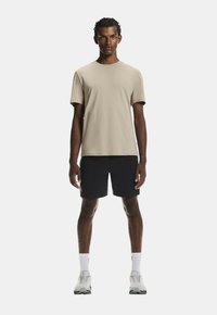 Béžové bavlnené tričko s krátkymi rukávmi, spárované s čiernymi šortkami. Model má na sebe biele športové topánky a biele ponožky do členkov.