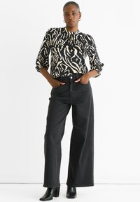 Black and cream patterned blouse with puffed sleeves, paired with high-waisted black wide-leg jeans and black heeled boots.