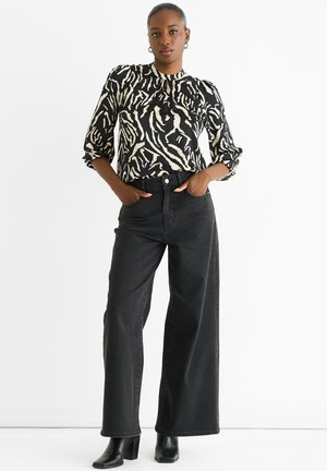 Black and cream patterned blouse with puffed sleeves, paired with high-waisted black wide-leg jeans and black heeled boots.