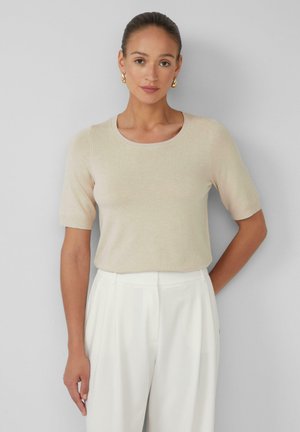 Helles beiges Kurzarm-Strickoberteil mit rundem Halsausschnitt. Kombiniert mit hochgeschnittenen weißen Hosen. Glatte Textur, taillierte Passform.