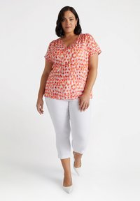 Blouse à manches courtes et décolleté en V arborant un motif floral rouge et orange vif, associée à un pantalon cropped blanc et des talons à bout pointu.
