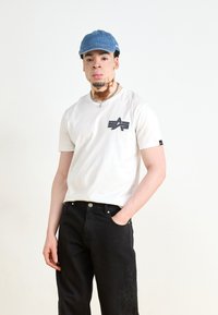 Hvit bomulls t-skjorte med en svart grafisk logo på brystet, kombinert med svarte denim bukser med blomsterbroderi på det ene benet.
