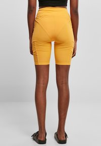 Gele hoge taille fietsbroek met een aansluitend ontwerp, een gladde textuur en zijnaaddetails, gecombineerd met zwarte sandalen.