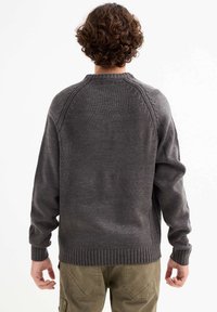 Suéter gris de punto con dobladillo y puños acanalados, que presenta un escote redondo y detalles de trenzado a lo largo de las costuras de los hombros.