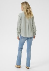 Camicia a righe verdi e bianche con maniche lunghe, abbinata a jeans a zampa d'elefante azzurri e zoccoli beige. Vista posteriore.