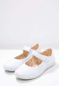 Białe lakierowane buty Mary Jane na rzep z kwiatowym wnętrzem, z okrągłym noskiem i niską gumową podeszwą.