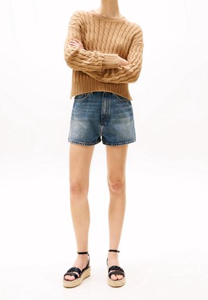 Pull en tricot beige avec un motif texturé, associé à un short en denim bleu. Sandales espadrilles noires avec un design tissé et une bride autour de la cheville.