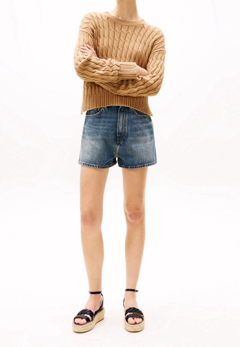 Pull en tricot beige avec un motif texturé, associé à un short en denim bleu. Sandales espadrilles noires avec un design tissé et une bride autour de la cheville.