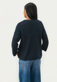 Pull en maille bleu marine foncé avec une coupe décontractée, col rond et manches trois-quarts, associé à un jean large bleu clair.