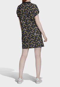 Černé šaty s květinovým vzorem, který obsahuje žluté a fialové květy. Krátké rukávy a volný střih. Nosené s bílými botami se zelenými akcenty.
