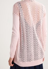 Ljusrosa stickad tröja med ett strukturerat mönster i öppen väv med zick-zack och diamantmönster, långa ärmar och en avslappnad passform.