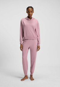 Rosa träningsset bestående av en hooded sweatshirt med avslappnad passform och matchande åtsittande sweatpants. Mjuk textur, minimalistisk varumärkesdetalj.