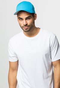 Blue cap with a curved visor, made of durable fabric. Worn with a plain white t-shirt. Visible seams and stitching details on the cap.