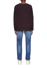 Dunkellila Langarmshirt mit rundem Ausschnitt, getragen mit hellblauen geraden Jeans und weißen Sneakers, von hinten betrachtet.
