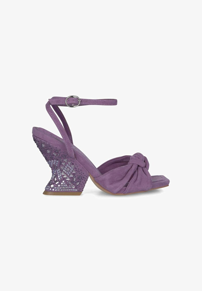 Sandal in suede viola con tacco a zeppa, caratterizzato da un dettaglio annodato sulla parte superiore e un tacco decorato con motivo geometrico. Cinturino alla caviglia con chiusura a fibbia.
