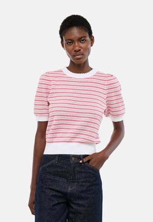 Femme portant un haut en maille à manches courtes rayé rose et blanc avec des épaules bouffantes et un jean taille haute foncé, main dans la poche.