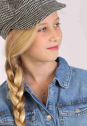Schwarz-weiße Hahnentritt-Mütze, geflochtenes blondes Haar, blaues Jeanshemd mit Metallknöpfen und eine silberne Halskette mit einem kleinen Türkis-Anhänger.