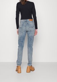 Pantalones vaqueros de denim azul claro con corte recto, acabado desgastado y dos bolsillos traseros con costura en zigzag. Combinados con zapatos de plataforma color marrón.
