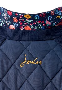 Tejido de algodón acolchado en color marino con forro de estampado floral, con bordado dorado de "joules". El cuello acanalado texturizado aporta contraste.
