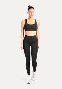 Svart atletisk crop top och höga tights i fukttransporterande material; modellen bär vita sneakers. Mjukt, åtsittande passform.