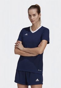 Tumedast lühikeste varrukatega spordijas, millel on valge V-kaelus. Rinnal on Adidas logo ja sellega sobivad lühikesed püksid. Kerge, sportlik lõige.