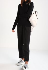 Černý pletený svetr s vysokým límcem, doplněný černými kalhotami s manžetami a metalickými stříbrnými teniskami. Bílá kabelka s zak�řiveným designem.