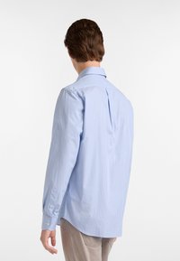 Camicia a strisce azzurro chiaro con maniche lunghe, polsini con bottone e una piega sul retro. Vestibilità sartoriale con orlo curvo.