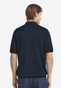 Marinblå kortärmad polo, avslappnad passform, ribbad krage och ärmslut, slät textur, bakdesign med detaljer vid axelsömmen.