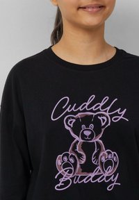 Czarna bluza z kapturem ma grafikę kreskówkowego niedźwiedzia w odcieniach brązu i różu oraz napis "Cuddly Buddy" w zabawnym kroju pisma. Miękka, casualowa tkanina.