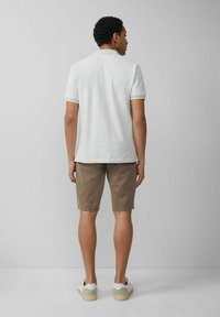 Weißes Polohemd mit kurzen Ärmeln und klassischer Passform, kombiniert mit khakifarbenen Shorts und weißen Sneakern mit hellen Akzenten; glatter Stoff, legerer Stil.