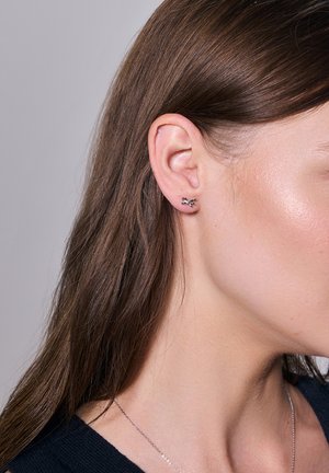 Srebrne kolczyki w kształcie motyla, o polerowanym wykończeniu i delikatnych detalach, noszone na uchu modelki.